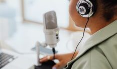 pexels-photo-5399007-5399007 Back view of a woman recording a podcast indoors using a microphone and headphones.